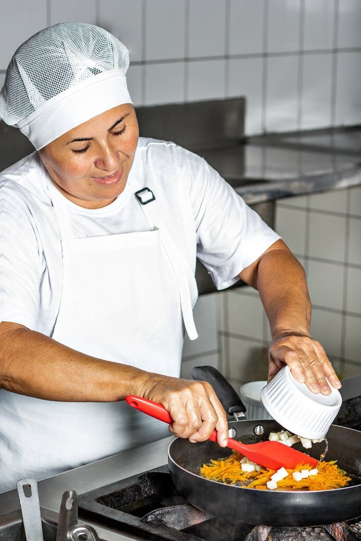 Cozinheira salteando temperos frescos na frigideira
